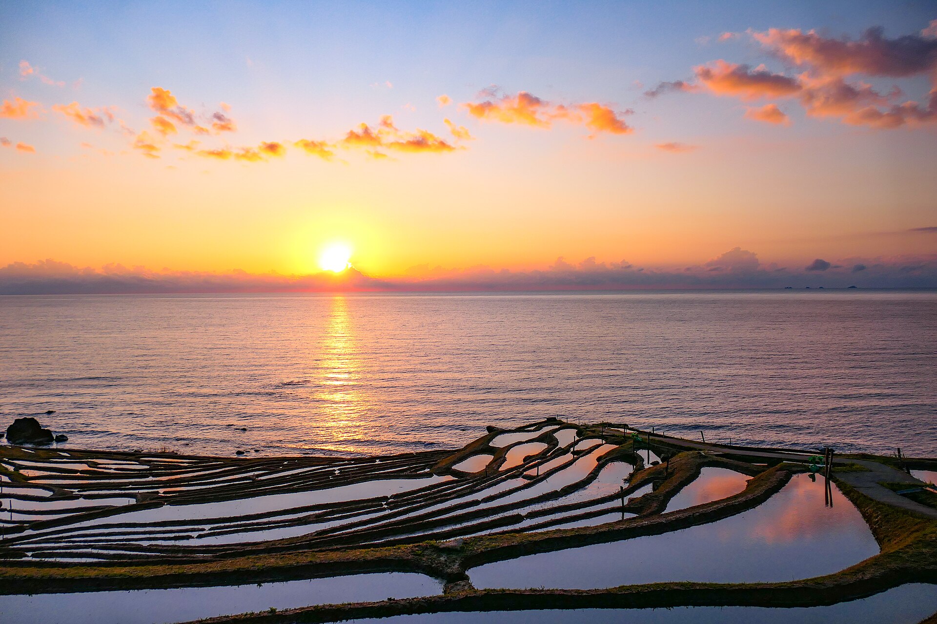 日本海に沈む夕日と白米千枚田の幻想的な風景
